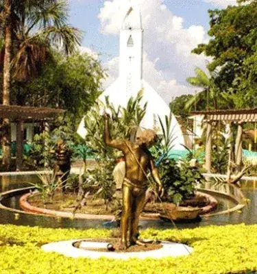 Iglesia blanca con torre alta detrás de una fuente con estatua dorada y nenúfares amarillos.