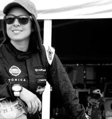 Manuela Vásquez con traje de piloto junto a su auto de carreras