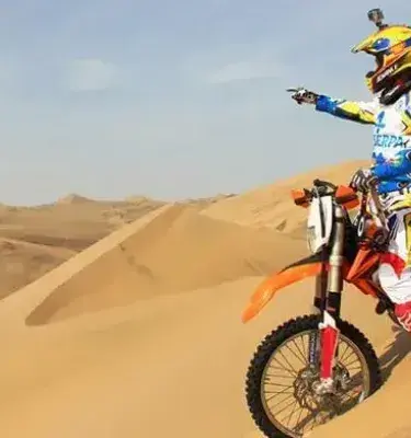 Motociclista colombiano en el Rally Dakar señalando el horizonte en el desierto