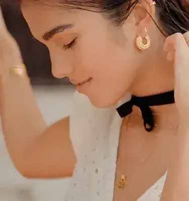 Mujer con pendientes y collar de oro, gargantilla negra y un tatuaje en el brazo.