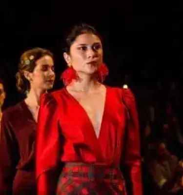 Woman wearing a red blouse and earrings on a dark catwalk.