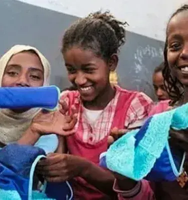 Niñas sonrientes mostrando toallas higiénicas reutilizables en un aula