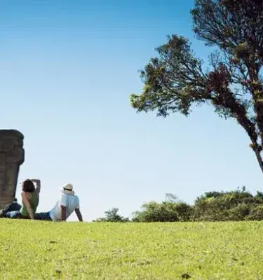 Pareja descansando en parque arqueológico con escultura ancestral y árbol