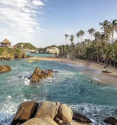 Tayrona Beach with palm trees and a hut on a rock.