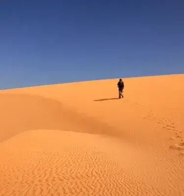 Persona camina dejando huellas en duna de arena dorada bajo cielo azul claro.