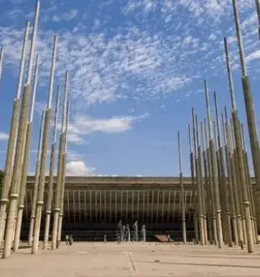 Plaza de Medellín con altos pilares de madera y cielo nublado.