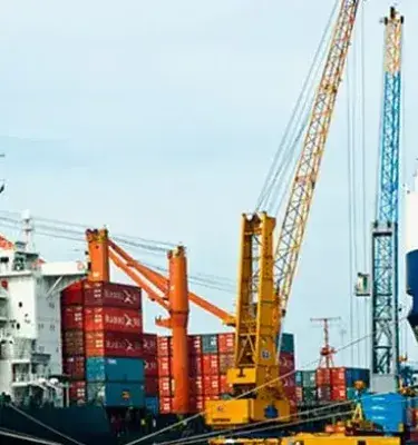 Puerto marítimo con un carguero de contenedores rojos y un gran buque azul, bajo grúas portuarias.