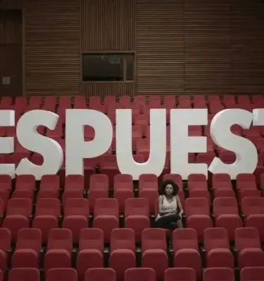 Mujer sentada frente a letras gigantes que forman la palabra RESPUESTA