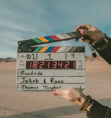 Dos manos sostienen una claqueta de cine en un paisaje desértico.