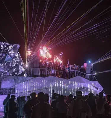 Escultura Jaguara iluminada con láseres y público en Burning Man de noche.