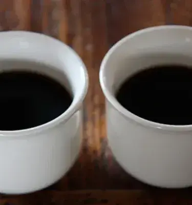 Dos tazas blancas llenas de café negro sobre mesa de madera.