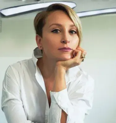 Mujer de cabello corto y camisa blanca posando con expresión pensativa