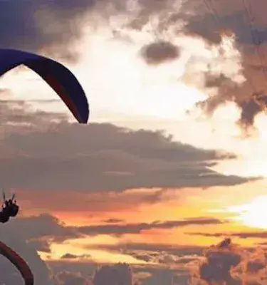 Personas practicando parapente al atardecer en el cielo colombiano
