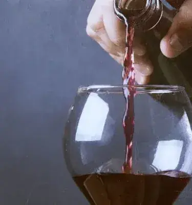 Primer plano de una mano sirviendo vino tinto en una copa de cristal.