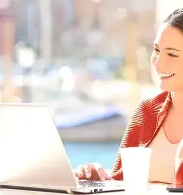 Smiling woman working on a laptop outdoors with a coffee