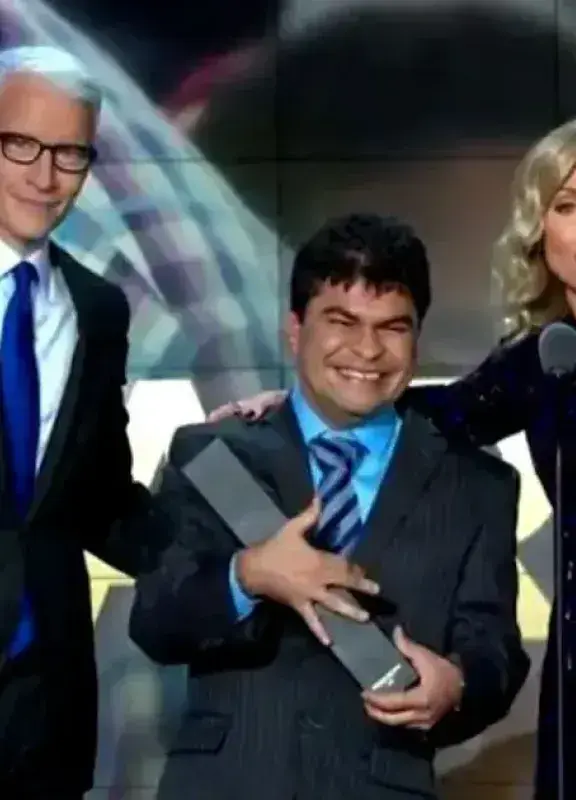 Anderson Cooper, un hombre sonriente sosteniendo un premio y Kelly Ripa en un escenario de gala.