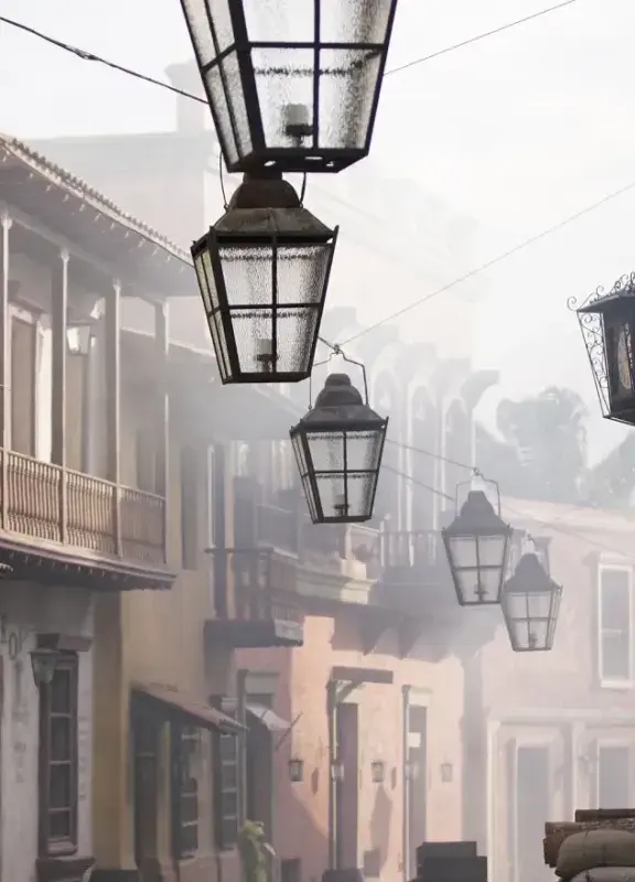 Calle antigua con balcones de madera y faroles colgantes, con ambiente de neblina que evoca un pueblo tradicional latinoamericano.
