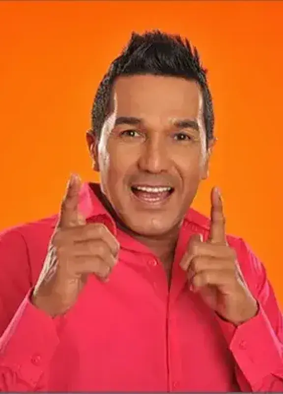 Hombre sonriente con camisa fucsia posando frente a fondo naranja
