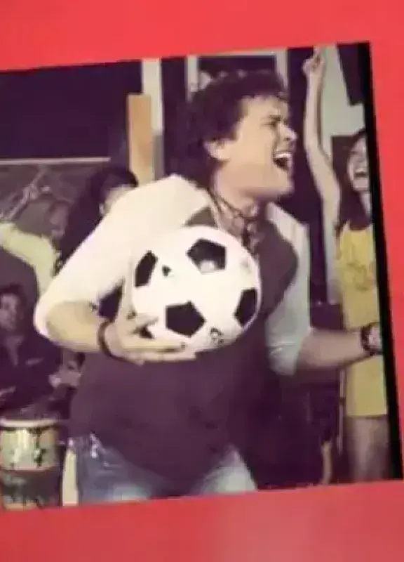 Cantante colombiano con balón de fútbol celebrando en un escenario colorido