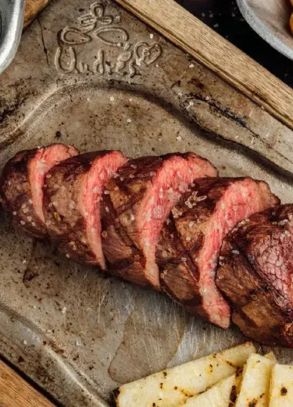 Lomo de res asado servido en rodajas con papas criollas y salsas típicas.