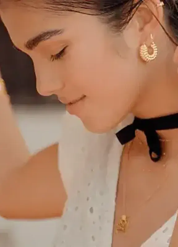 Mujer con pendientes y collar de oro, gargantilla negra y un tatuaje en el brazo.