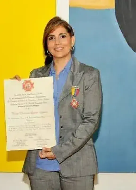 Mujer recibiendo reconocimiento con diploma y medalla frente a pinturas coloridas