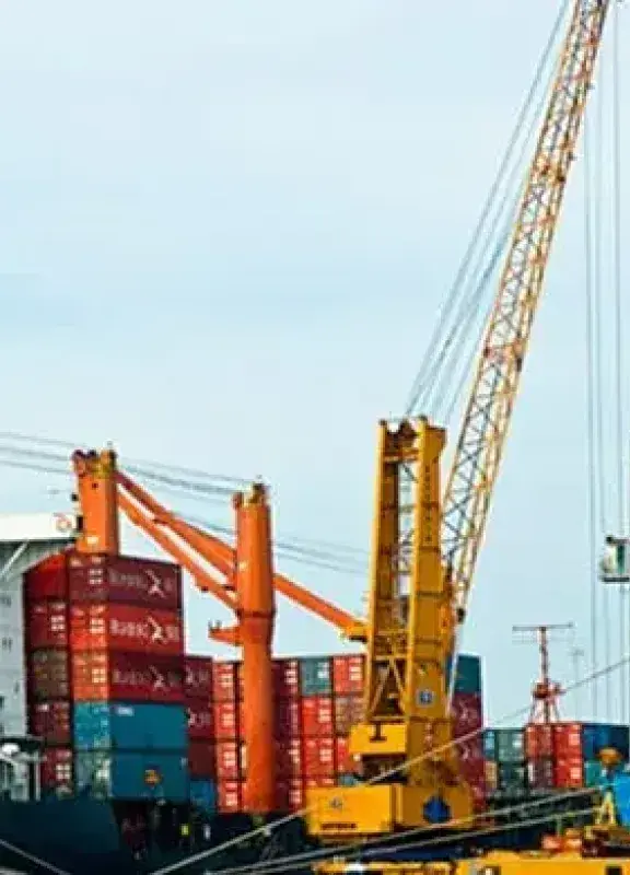 Puerto marítimo con un carguero de contenedores rojos y un gran buque azul, bajo grúas portuarias.