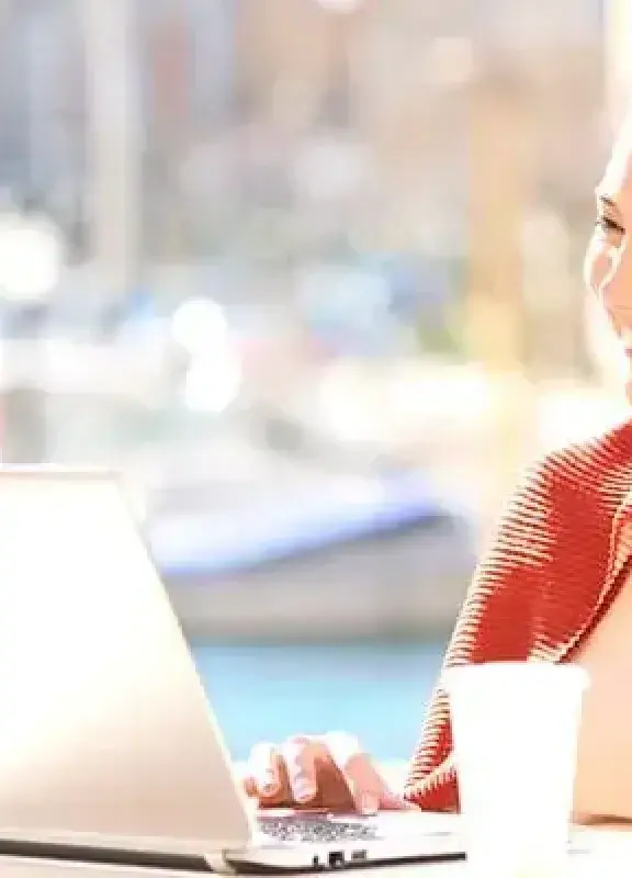 Smiling woman working on a laptop outdoors with a coffee