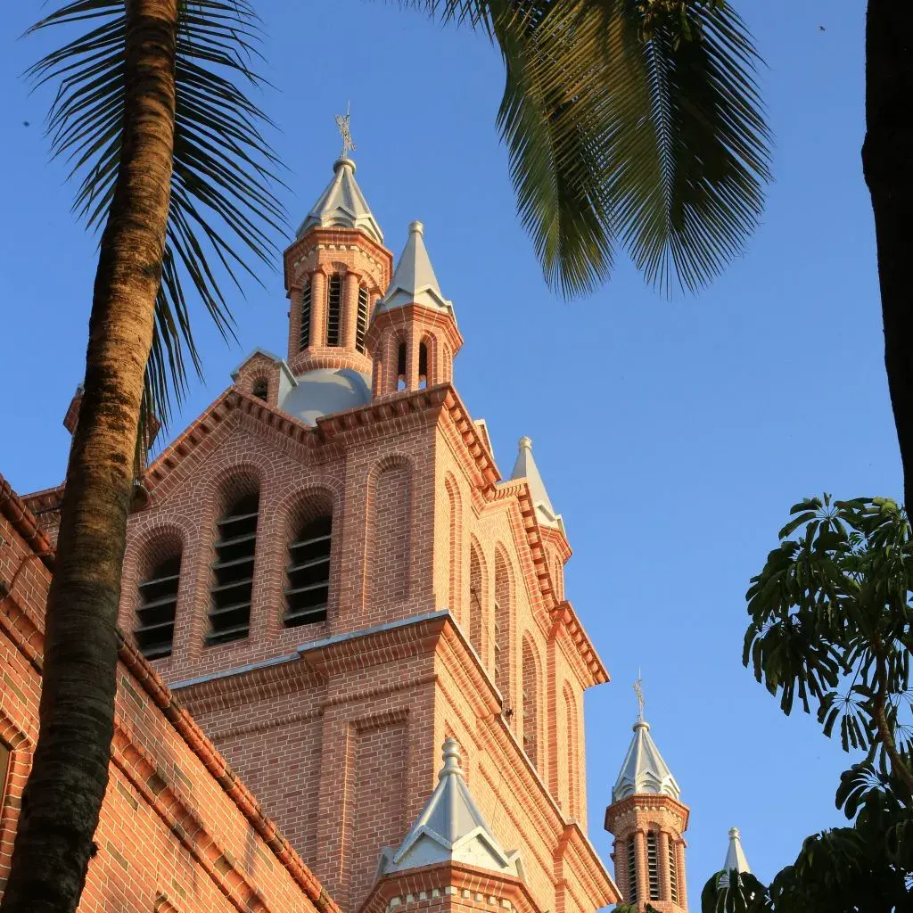 Fachada de ladrillo de la Basílica de Buga con palmeras en primer plano.
