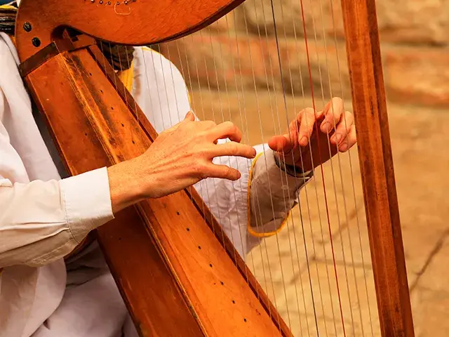 Manos tocando un arpa de madera con cuerdas, vista cercana y detallada.