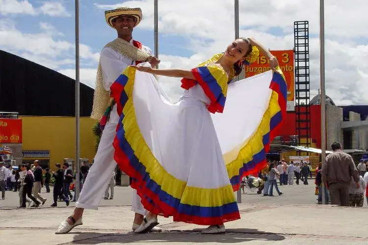 Pareja bailando cumbia con trajes tradicionales de Colombia en un espacio público.