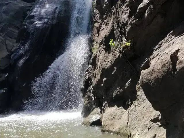 Cascada entre rocas oscuras y un pequeño estanque de agua.