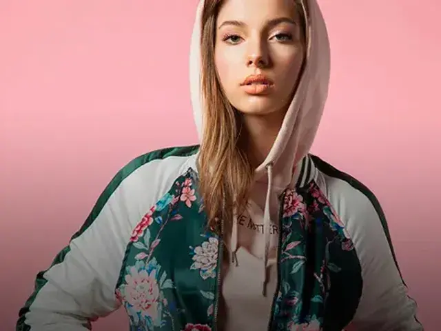 Mujer con chaqueta floral y capucha, mirando a la cámara con expresión seria.