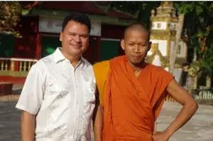 Dos hombres, uno con túnica naranja, posando juntos.