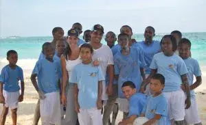 Grupo de niños y adultos en la playa, vestidos de azul y blanco.