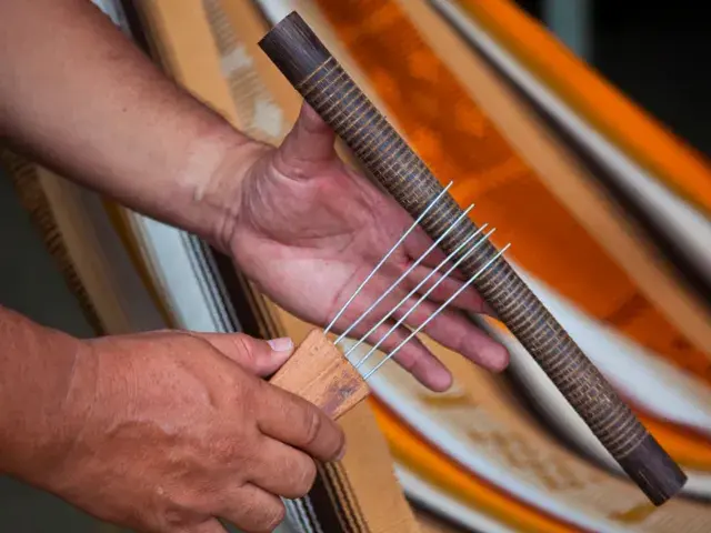 Manos sosteniendo una guacharaca, instrumento musical de fricción con ranuras.