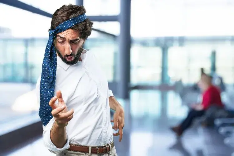 Hombre con corbata en la cabeza haciendo gestos de borracho en un espacio público