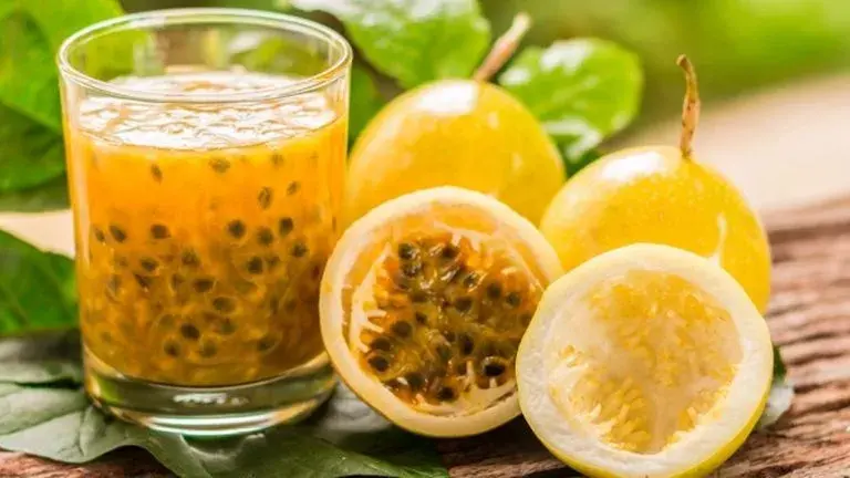 Passion fruit juice in glass with whole and cut yellow passion fruit.