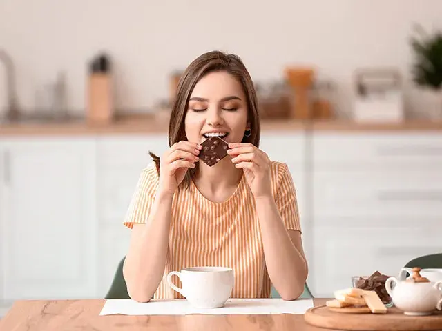 Mujer disfrutando un trozo de chocolate en la mesa.