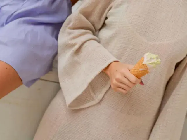 Persona con túnica beige sosteniendo un cono de helado derretido junto a otra persona con ropa lila.