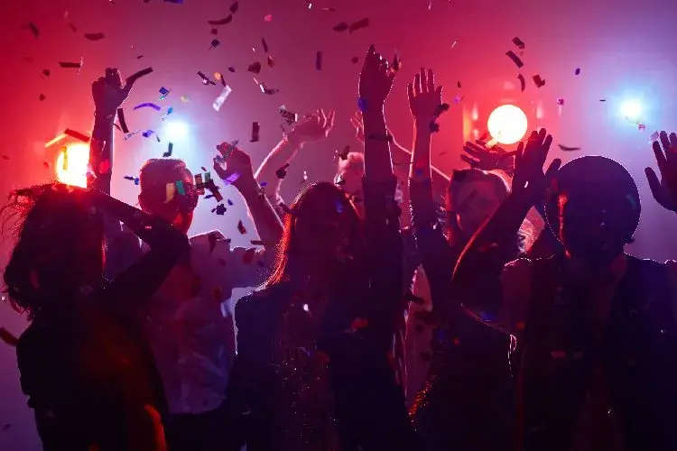 Grupo de personas disfrutando de una fiesta con luces de colores y confeti en el aire