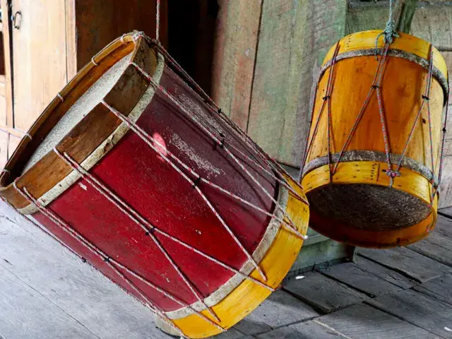 Dos tambores tradicionales de madera, uno rojo y otro amarillo, colgando en un interior rústico.