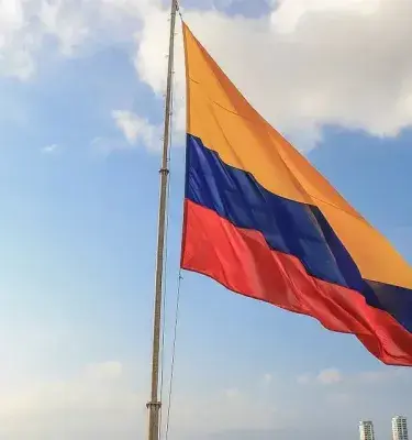 Colombian flag flying against a blue sky with clouds.