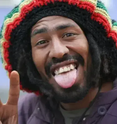 Hombre con gorro rastafari sacando la lengua y haciendo la señal de paz.